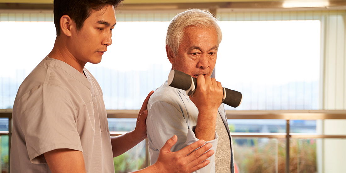 Physiotherapist assisting an elderly man with seated exercises.