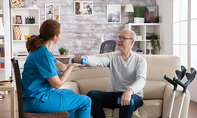Physiotherapist helping an elderly woman with dumbbell exercises.