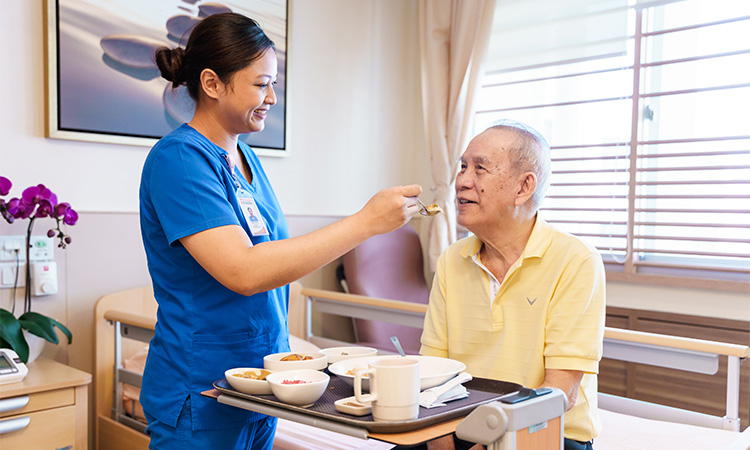 Caregiver feeding elderly man in nursing home.