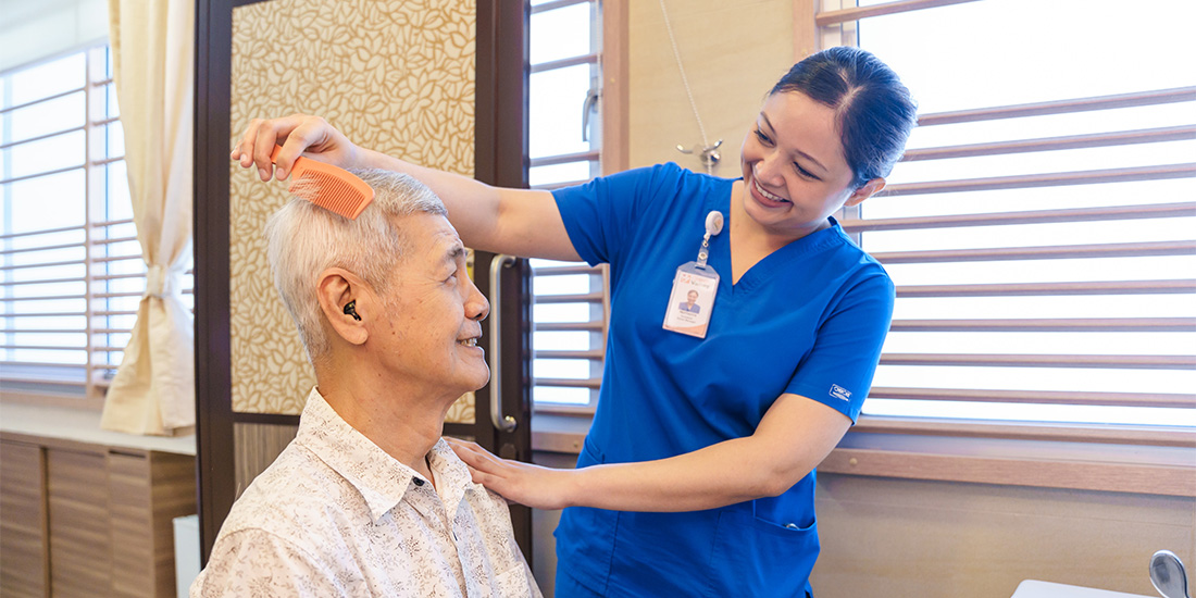 Caregiver combing elderly man's hair in nursing home.