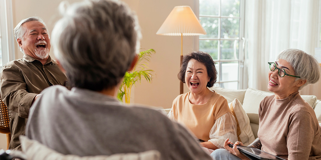 Group of happy seniors laughing together in a living room.