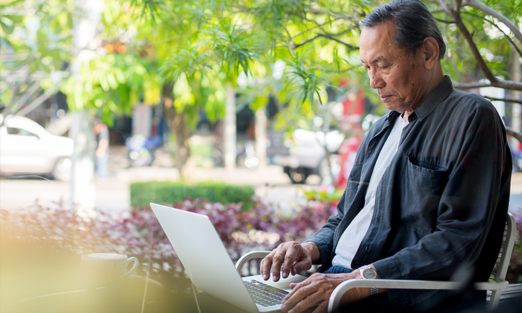 Senior man using a laptop outdoors to stay connected.